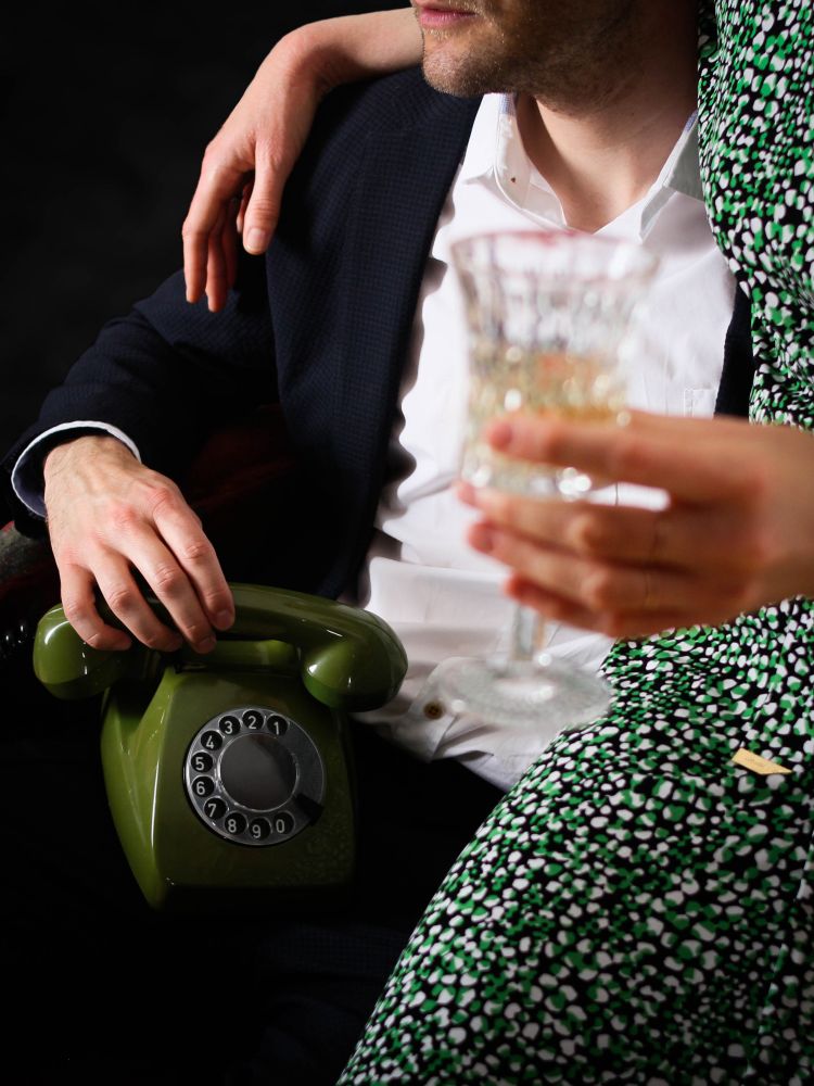Ein grünes Telefon von Quasselstrippe auf einer Party - im Vordergrund ist ein Sektglas zu sehen.